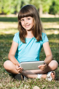 Onun tablet bilgisayar ile parkta oturan küçük kız