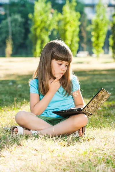 Bella bambina seduta nel parco con il suo computer portatile — Foto Stock