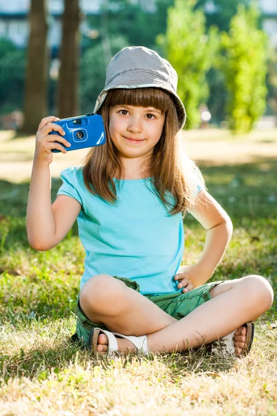Chica sentada en el parque y sosteniendo la cámara fotográfica — Foto de Stock