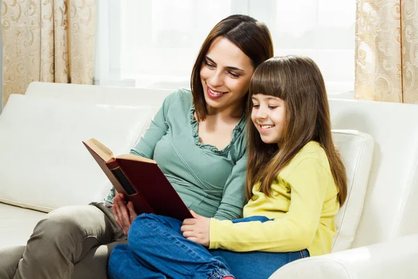 Madre e hija sentadas en un sofá y leyendo un libro —  Fotos de Stock