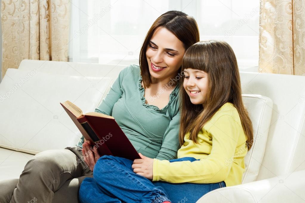 Mother and daughter sitting on sofa and reading a book