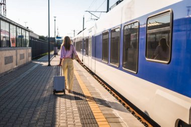 Şık bir iş kadınının bavulu çekişi ve tren istasyonunda yürüyüşü günlük şehir seyahatinin özünü yansıtıyor..