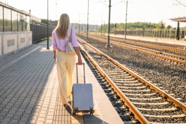 Tren istasyonunda bavulla yürüyen zarif bir iş kadınının arka görüntüsü. İş gezisine gidiyor..