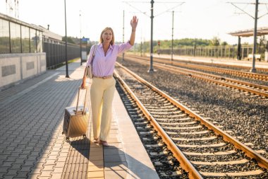 Endişeli bir iş kadını, ayrılan bir trene el sallıyor ve tren istasyonunda bavullarıyla koşuyor..