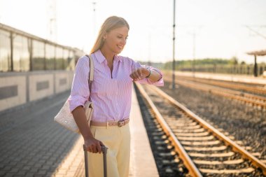 Tren istasyonunda durup kol saatine bakan güzel, zarif bir iş kadını. Trenin gelişini bekliyor..