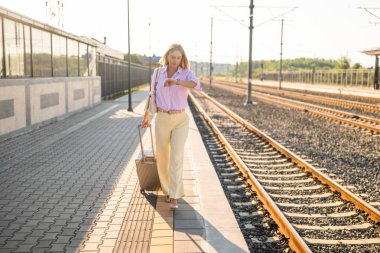 Tren istasyonunda yürürken kol saatine bakan bavullu, kendinden emin ve zarif bir iş kadını. İş gezisine gidiyor..