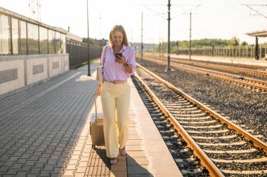 Tren istasyonunda yürürken cep telefonu kullanan kendine güvenen bir iş kadını. Bağlantı, teknoloji ve iş hareketliliğini temsil eder.
