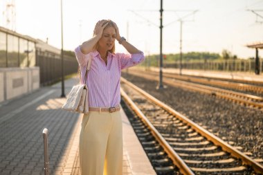 Tren istasyonunda bekleyen, bavullu hoşnutsuz iş kadını. Ulaşım sorunlarından dolayı çok üzgün..
