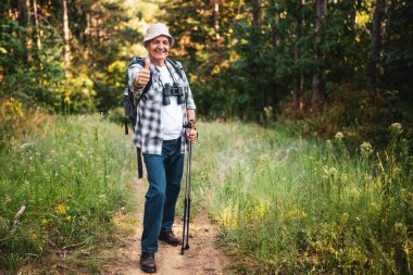 Dağlardaki açık hava macerası sırasında baş parmağını gösteren mutlu yaşlı yürüyüşçünün portresi..
