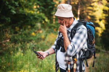 Yaşlı yürüyüşçü ormanda kaybolmuş, rehberlik için akıllı telefonunu kontrol ediyor..