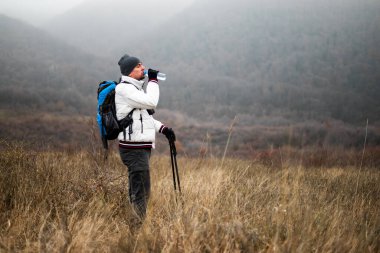 Sırt çantalı ve yürüyüş direkli yürüyüşçü sisli kış günlerinde dinlenmek ve su içmek için mola veriyor..