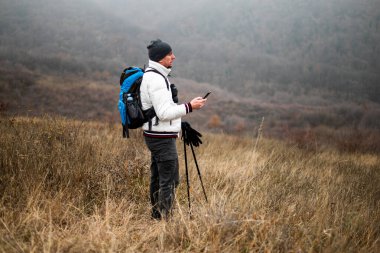 Sırt çantalı, yürüyüş direkleri olan, sisli kış günlerinde doğa yürüyüşü yaparken akıllı telefon kullanan bir yürüyüşçü. Keşif ve teknolojiyi birleştirerek, açık havada macera ve eğlence peşinde koşuyor..