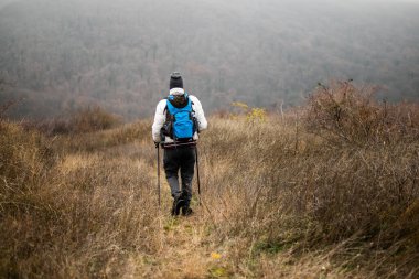 Yürüyüşçünün sisli dağ manzarasında kış yürüyüşünün keyfini çıkardığı dikiz manzarası. Sıcak kıyafetler giyip sırt çantası ve yürüyüş direği taşıyarak doğayı, macerayı ve özgürlüğü kucaklıyor..