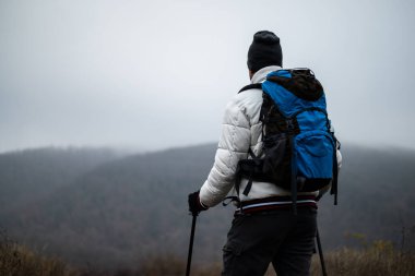 Sırt çantalı, yürüyüş direkleri olan, kış günü sisli dağlarda yürüyüş yapan doğa, canlılık ve aktif eğlence aktivitelerini kucaklayan bir yürüyüşçü..