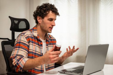 Oturma odasında oturan genç bir adam dizüstü bilgisayarından sağlık hizmeti uzmanıyla iletişim kuruyor, tıbbi durumunu ve tedavi seçeneklerini tartışıyor. Teletıp kavramı.