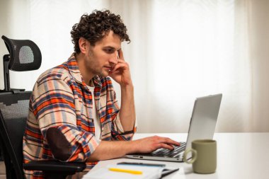 Başarılı genç iş adamı dizüstü bilgisayarını kullanıp rahat evinde uzaktan çalışıyor..