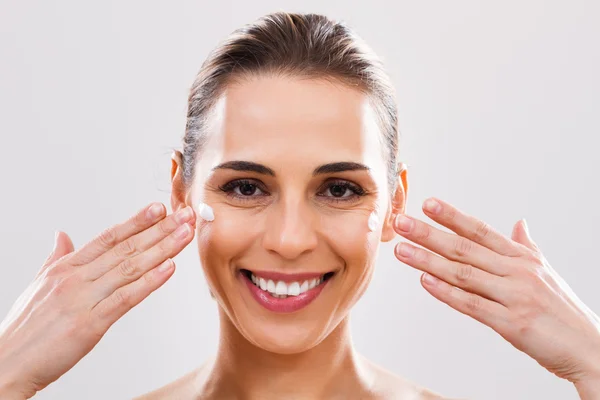 Vrouw vochtinbrengende crème toe te passen op gezicht — Stockfoto