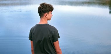 Mavi bir gölün önünde üzgün görünen genç bir beyaz adam.
