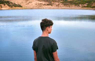 Mavi bir gölün önünde üzgün görünen genç bir beyaz adam.