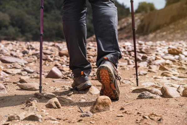 Man hiking along stone path with hiking shoes and walking poles. Man hiking on sand and stones path near mountains.
