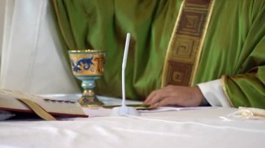 Yeşil cüppeli rahip kilise sunağının yanında duruyor ve kutsal kitabı okuyor. Yerel papaz, ayinle ilgili vaaz veriyor ve insanlarla birlikte Tanrı 'ya dua ediyor. Din ve katolik