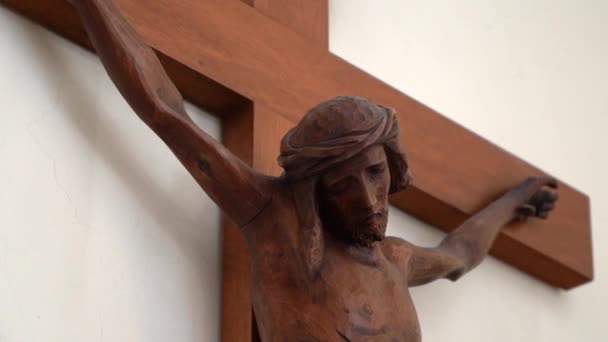 耶稣基督十字架的木制雕像挂在教堂的白墙上，十字架上的耶稣饰物头上戴着荆棘花环，血淋淋。神的儿子在十字架上为人类的罪而死，耶稣在十字架上受苦 — 图库视频影像