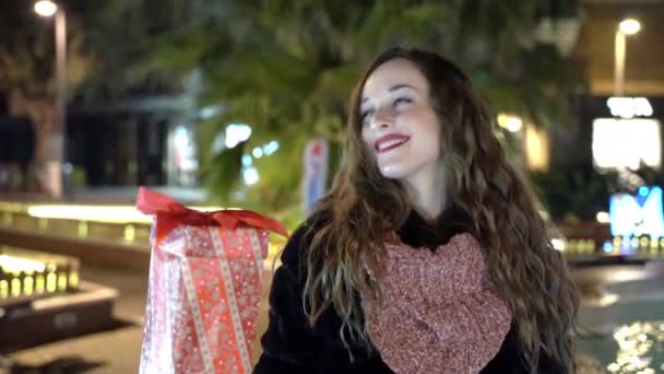 Vacker kvinna med bedårande ögon som håller julklapp i händerna och dansar på fantastisk upplyst gata bakgrund, glad kvinna njuter vinterkväll utomhus i parken och visar uppriktig — Stockvideo