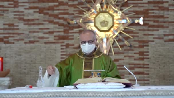 CASSINO, ITALIA - 18 DE OCTUBRE DE 2020: Misa eclesiástica en la ciudad provincial italiana de Cassino, sacerdote de mediana edad con mascarilla protectora acercándose al altar para la preparación de la ceremonia. Pastor vertiendo agua sagrada — Vídeo de stock