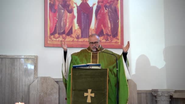 CASSINO, ITALIEN - OKTOBER 18, 2020: Italiensk lokal präst står på bakgrund av religiös ikon i kyrkan och håller predikan med hjälp av heliga Skriften och mikrofon, pastor ber för bit i världen — Stockvideo