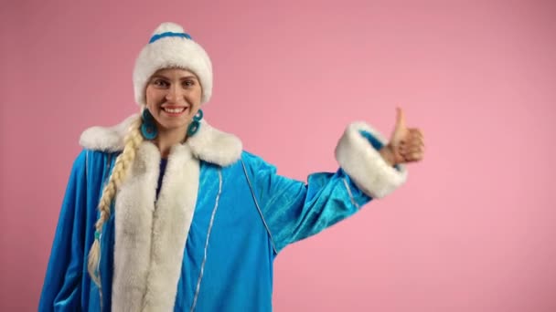 Feliz mujer sonriente en traje de navidad azul de pie sobre fondo rosa, mirando a la cámara y mostrando el pulgar hacia arriba. Alegre doncella de nieve mostrando gesto positivo, mujer emocionada y signo de felicidad — Vídeo de stock