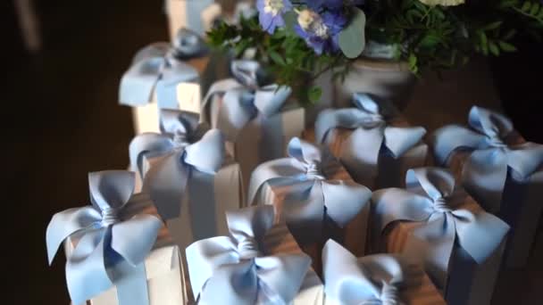 Прекрасные праздничные услуги на банкетном столе с цветочным букетом в центре, маленькие белые бумажные коробочки с голубой лентой, приготовленные для крещения. Сладкие конфетти в коробках Bonbonniere, спасибо — стоковое видео