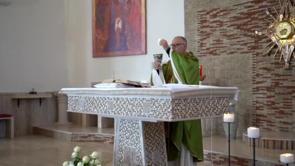 CASSINO, ITALIË - OKTOBER 18, 2020: Italiaanse priester van middelbare leeftijd die naast het kerkaltaar staat en kelk met sacramenteel brood in handen houdt, pastoor die de Heilige Schrift leest, God bidt en — Stockvideo