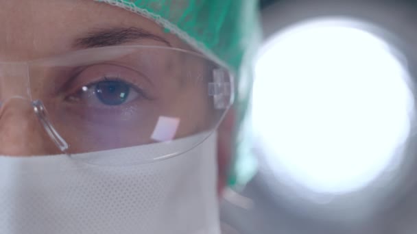 Vermoeide ogen van een zelfverzekerde arts die op camera kijkt op een heldere achtergrond in het lab. Close-up gezicht van een vrouw met een medische bril en masker, werkzaam in het ziekenhuis tijdens het coronavirus — Stockvideo