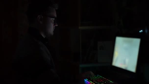 Gözlüklü bir gencin karanlık bir odada yanıp sönen ışıklarla oturduğu ve modern güçlü bilgisayarla bilgisayar oyunları oynadığı bir yan görüntü. Genç profesyonel oyuncu nişancı — Stok video