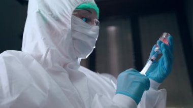 Bilimsel araştırma laboratuvarında zor kimyasal deneyler, koruma altında biyofizikçi kırmızı rengin tehlikeli çözümü ile çalışıyor, şırıngayı şişeden dolduruyor ve test için hazırlanıyor.