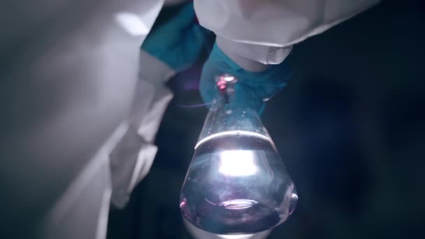 Esperimenti di rischio in laboratorio di ricerca, primo piano del bicchiere di vetro con liquido trasparente sulla luce di contrasto. Scienziato in guanti protettivi e tuta caduta di sangue all'interno del pallone per — Video Stock