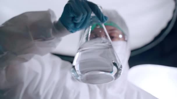Experimentos de pesquisa biotecnológica em laboratório, cientista em macacão protetora trabalhando com soluções líquidas de risco em copo estéril transparente, realizando diferentes experimentos químicos — Vídeo de Stock
