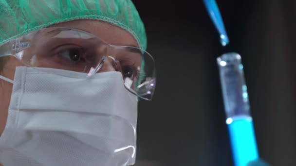 Γυναίκα εργαστηριακή υπάλληλος με προστατευτική μάσκα και γυαλιά που κρατούν επιστημονικά πειράματα χρησιμοποιώντας μπλε αντιδραστήριο, χημικά στοιχεία και σύνολο ιατρικών οργάνων. Βιοφυσικός που ψάχνει τον τρόπο να αναπτυχθεί — Αρχείο Βίντεο