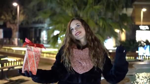 Mujer alegre bailando en el parque con regalo de Navidad en las manos, felicidad y emociones alegres durante las vacaciones de invierno. Concepto especial de regalo de Navidad — Vídeo de stock