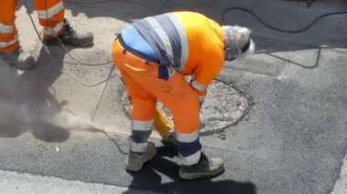 Koruyucu turuncu üniformalı takım çalışanları kanalizasyon rekonstrüksiyonu için asfaltı yok etmek için sondaj makinesi kullanıyorlar. Güçlü bir elektrikli matkap ile çimento temizleme. Modern kullanan işçiler