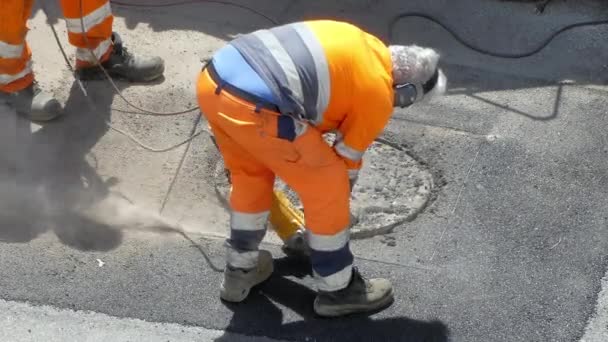 Teamworkers in protective orange uniform using drilling machine for destroying road asphalt for sewerage reconstruction, cement removal with powerful electric drill machine. Workmen using modern — Stockvideo