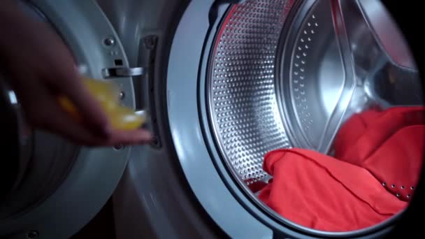 Rutinmässig hygien koncept, process för att ladda elektrisk tvättmaskin innan du slår på. Oigenkännlig kvinna kastar tre gula flytande kapslar inuti tvättmaskinen cylindern och stänga dörren — Stockvideo
