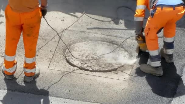 Drilling works on the construction site, unrecognizable workers in orange uniform breaking asphalt with electric cutting machine causing dust pollution in the city. Men using drilling tools for — ストック動画