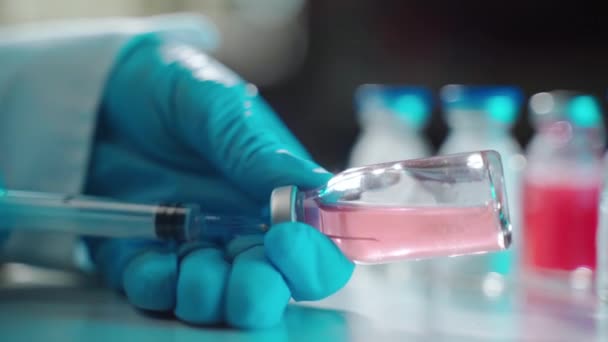Químico de laboratorio en guantes protectores llenando jeringa con solución de color rojo claro a partir de un vial transparente, investigador profesional que lleva a cabo experimentos químicos para desarrollar la vacuna contra el coronavirus — Vídeos de Stock