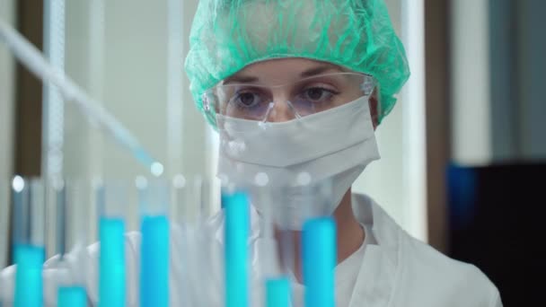 Συγκεντρωμένη γυναίκα ιατρικός επιστήμονας σε προστατευτικά γυαλιά, γάντια και κοστούμι κρατώντας ιατρικά πειράματα στην ανάπτυξη δυνητικού εμβολίου coronavirus, ιολόγος χρησιμοποιώντας διαφορετικά χημικά αντιδραστήρια για — Αρχείο Βίντεο