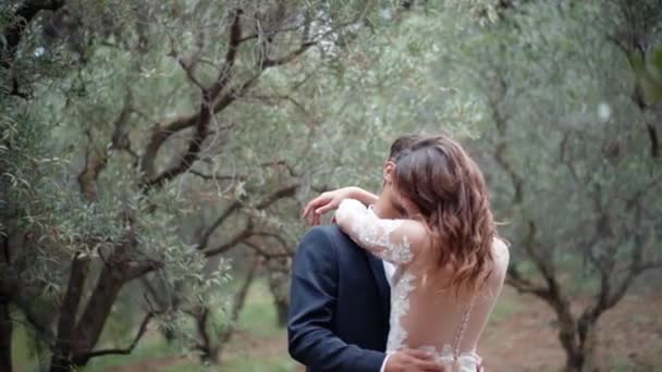 Young couple hugging and kissing in amazing olive trees garden, woman in white dress hugging her man and showing real lovely romantic emotions. Harmony in relationship, happiness in family — стоковое видео
