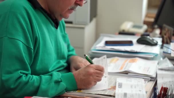 Senior financial worker in glasses sitting at the table, reading contract and putting his signature on sheet of paper. Process of signing agreement in bank department — 图库视频影像