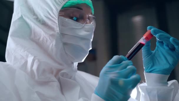 Conceito de microbiologia e virologia, cientista de laboratório em macacão protetora segurando tubo de teste de plasma sanguíneo em mãos e lendo dados escritos. Análise do plasma sanguíneo de doentes infetados com — Vídeo de Stock