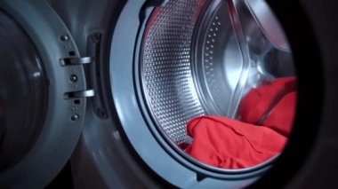 Çamaşır makinesinin santrifüjüne sarı sıvı granülü koyup kapıyı kapatan bir kadın eli. Evetyday rutin ev işleri, elektrikli çamaşır makinesi yükleme süreci