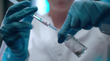 Female doctor in protective blue gloves infusing transparent substance inside the vial with powder, mixing chemical elements for developing effective vaccine against coronavirus infection. Vaccine